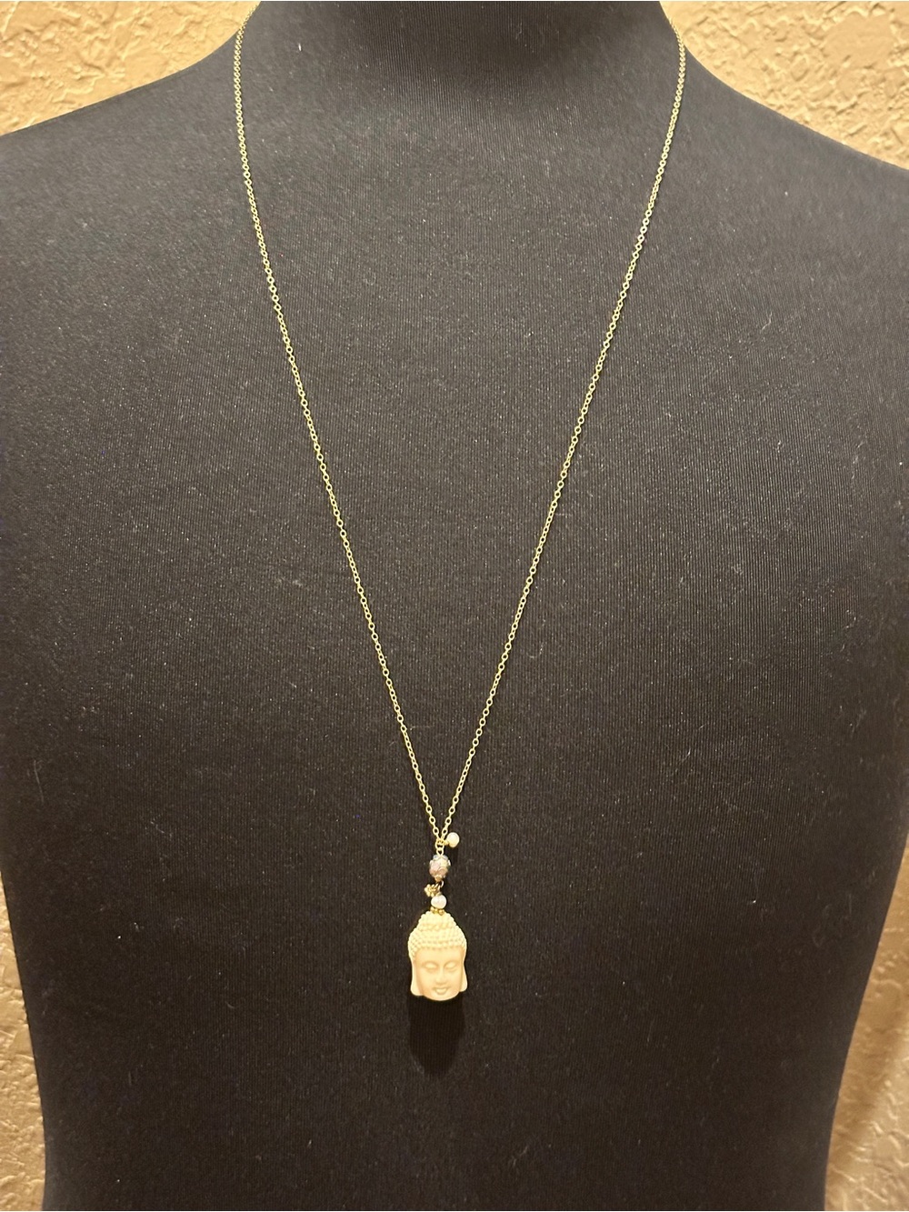 Long gold-tone chain necklace featuring a carved white bone or stone Buddha head